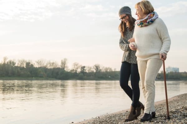 Older patient walking with a cane assisted by younger woman